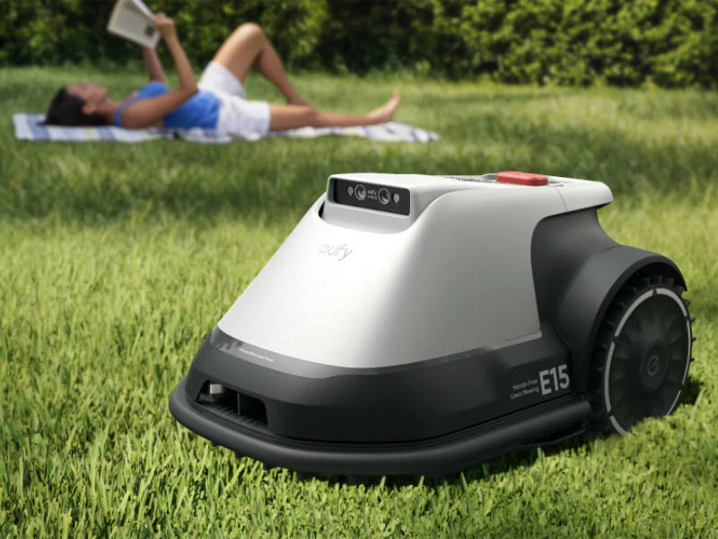 Eufy E15 fährt auf dem Rasen, Frau liegt auf Handtuch im Hintergrund
