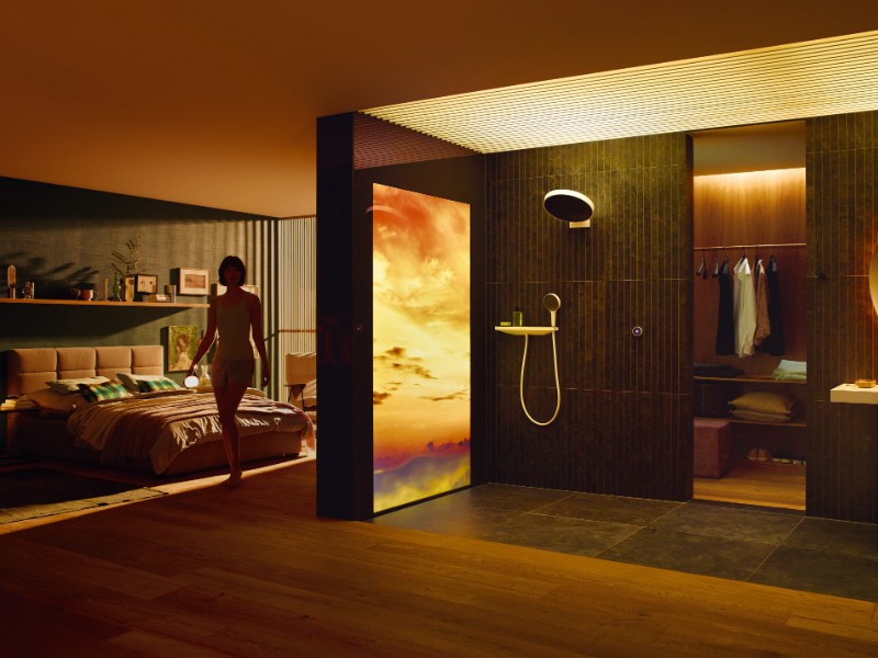 Ein stimmungsvolles Interieur mit warmer Beleuchtung, in dem eine Frau an einem Lichtpaneel mit einem lebhaften orange-violetten Sonnenuntergang vorbeigeht, was den Übergang zu den dunkleren Abenden nach dem Ende der Sommerzeit und dem Beginn der Winterzeit unterstreicht.