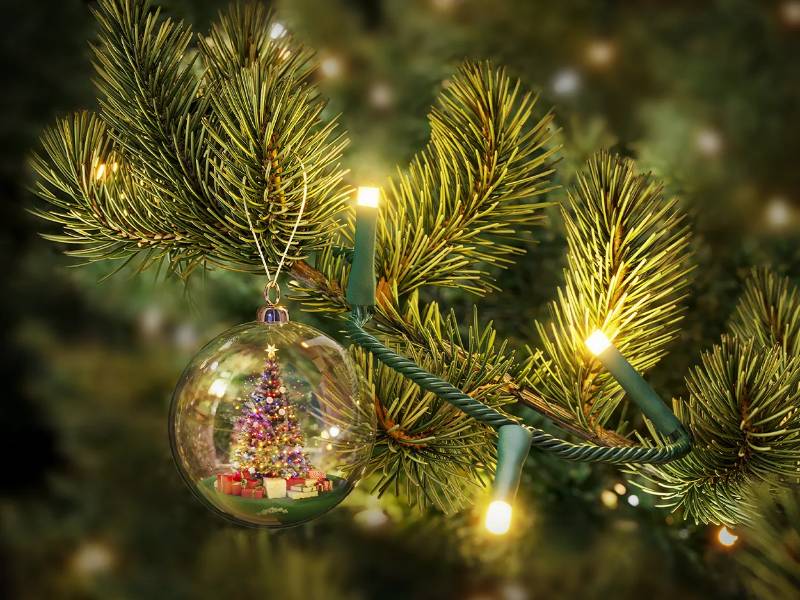 Nahaufnahme von dunkelgrünen Weihnachtsbaumzweigen mit warmweißer LED-Beleuchtung und einer gläsernen Weihnachtsbaumkugel