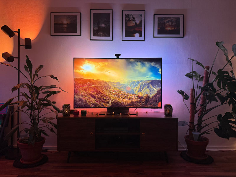 Fernseher zeigt atemberaubende Landschaft mit Sonnenuntergang links und blauem Himmel rechts; Govee TV-Backlight leuchtet den Hintergrund akkurat aus.