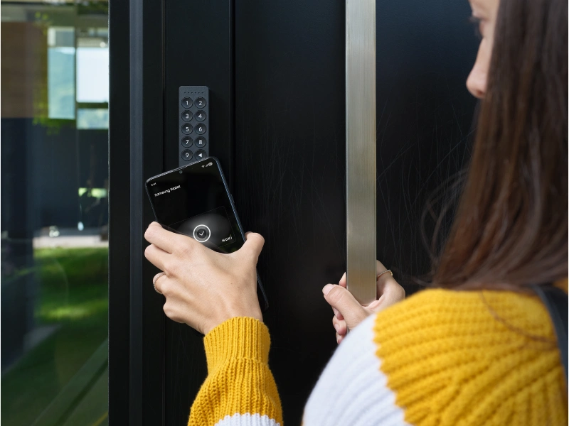 Frau entsperrt Nuki Keypad 2 NFC an der Haustür dank Aliro via Tap to unlock mit der Nuki App auf dem Smartphone