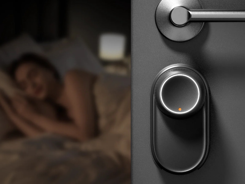 Dichromatisches Bild des SwitchBot Lock Ultra im Nachtmodus an einer dunklen Tür neben einem silbernen Türgriff mit einer orangefarbenen Kontrollleuchte; links ist verschwommen eine schlafende Person im Bett zu sehen. Der Schließhaken erzeugt weniger als 20 dB Geräusch.