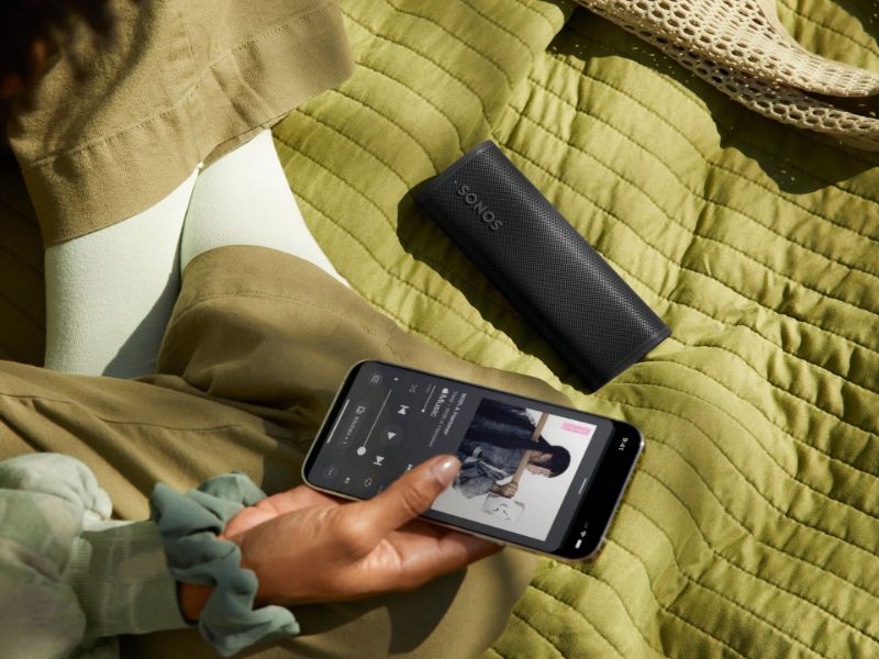 Ein schwarzer tragbarer Sonos-Lautsprecher und ein Smartphone auf einer grünen Decke, die die Vielseitigkeit eines zukunftssicheren Smart Homes veranschaulichen.