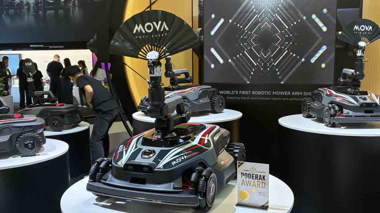 Mova AstraX auf einer Austellfläche auf der IFA 2026 - der Mähroboter steht auf einem Podest zusammen mit mehreren baugleichen Modellen. Alle haben den modularen Greifarm, der einen Fächer mit dem Mova-Logo hält.