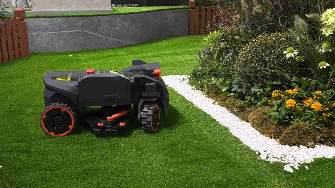 Segway Navimow H5 Pro Mähroboter fährt auf einer Demonstrationsfläche auf der IFA 2026 mit Rasen, Kiesrändern und Sträuchern in der Mitte. Der Seitenarm zum Kantenmähen ist ausgefahren.