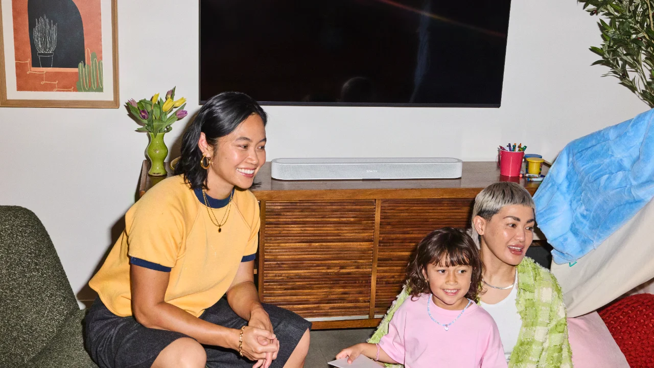 Zwei Frauen mit Kind im Wohnzimmer, im Hintergrund der Fernseher mit einer weißen Sonos Beam Ultra  auf dem TV-Schrank.