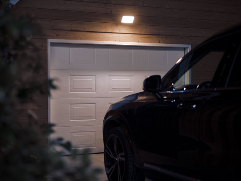 Es ist Nachts. Ein Auto steht vor einer geschlossenen Garage. Die Einfahrt wird Du die Philips Hue Flutlichtlampe erhellt.