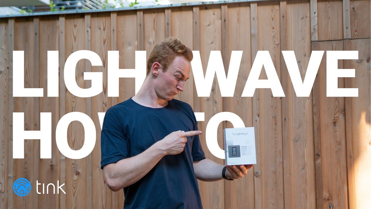 Mann vor einem Zaun zeigt auf die Verpackung des Lightwave Smart Dimmer