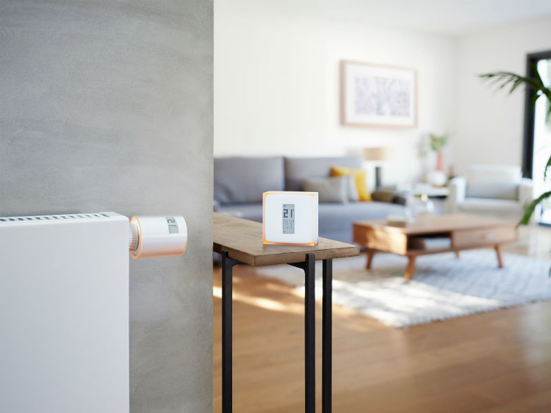 Netatmo Heizthermostat an Heizung und Raumthermostat auf Tisch daneben.