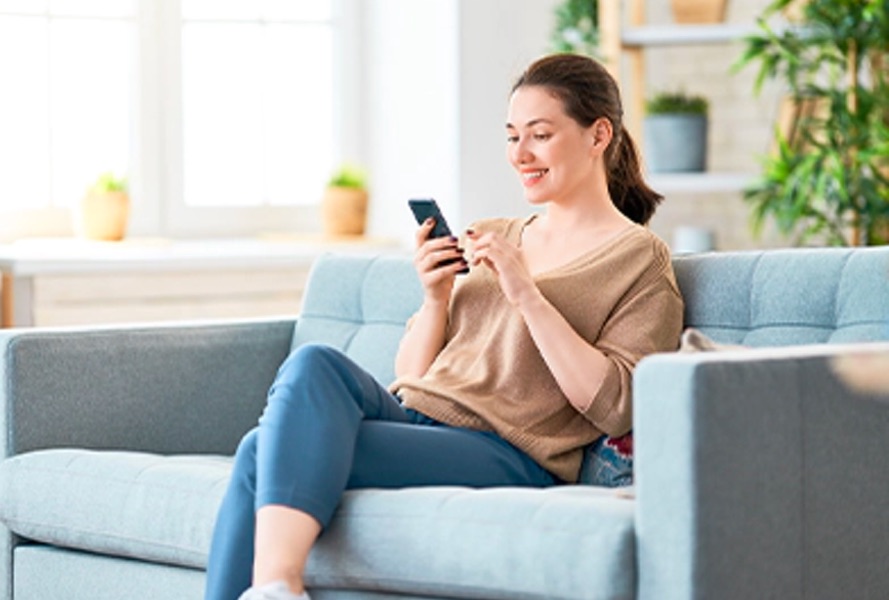 Frau sitzt auf dem Sofa mit ihrem Smartphone und nutzt die Google Home App