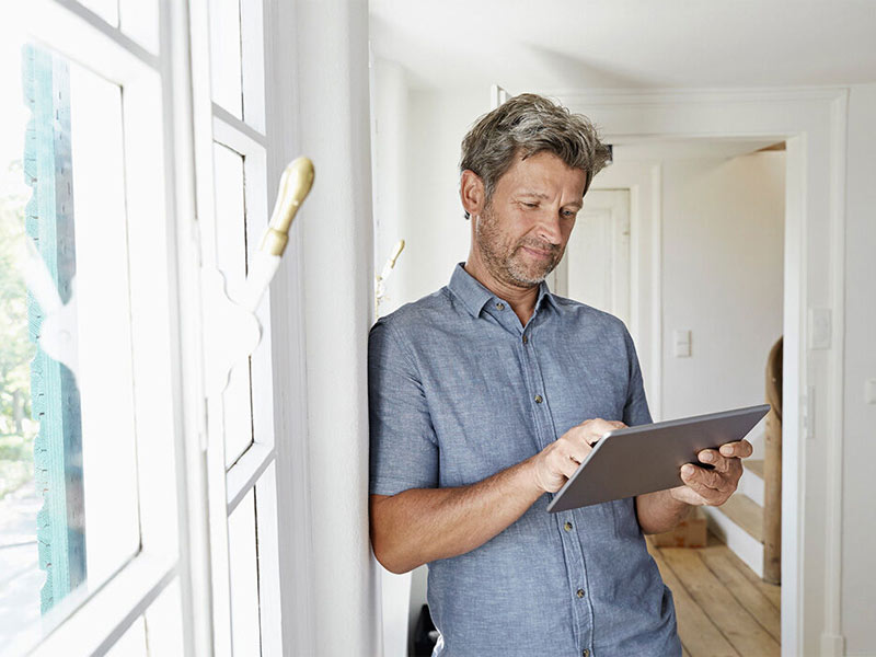 Mann steht im Flur und schaut auf sein Tablet