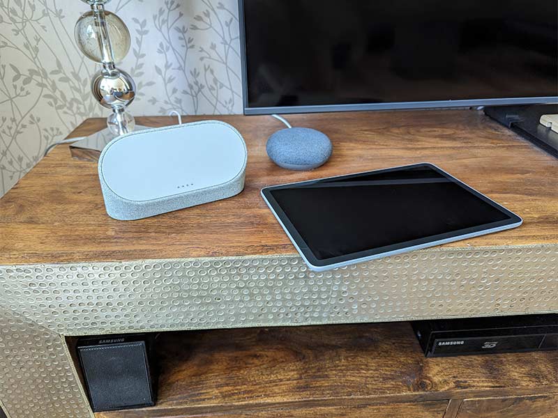 Pixel Tablet liegt neben dem Ladedock auf TV-Schrank mit Nest Mini