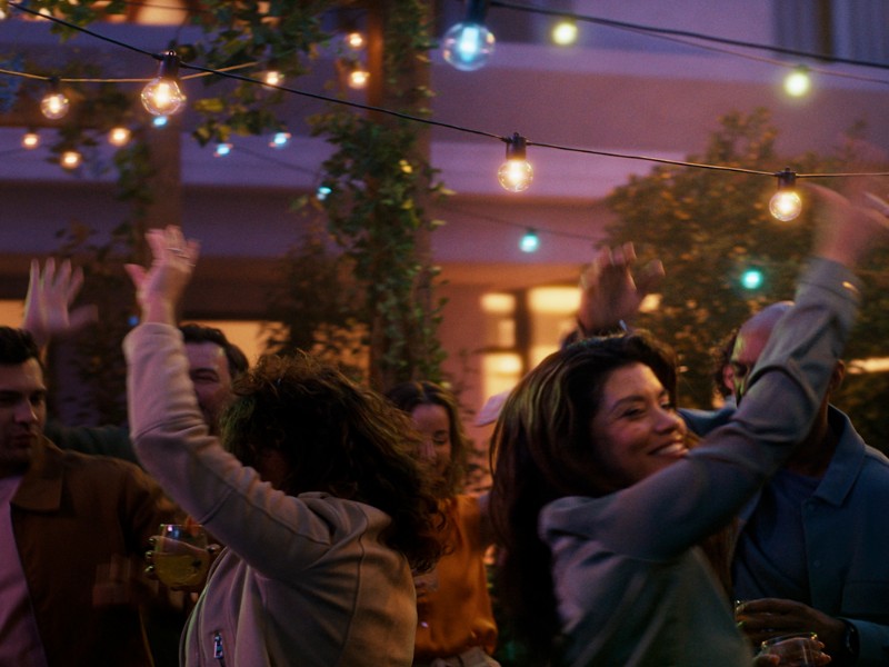 Slingerlampen met Nieuwe Philips Hue Lampen verlichten dansende mensen op een sfeervol buitenfeest.