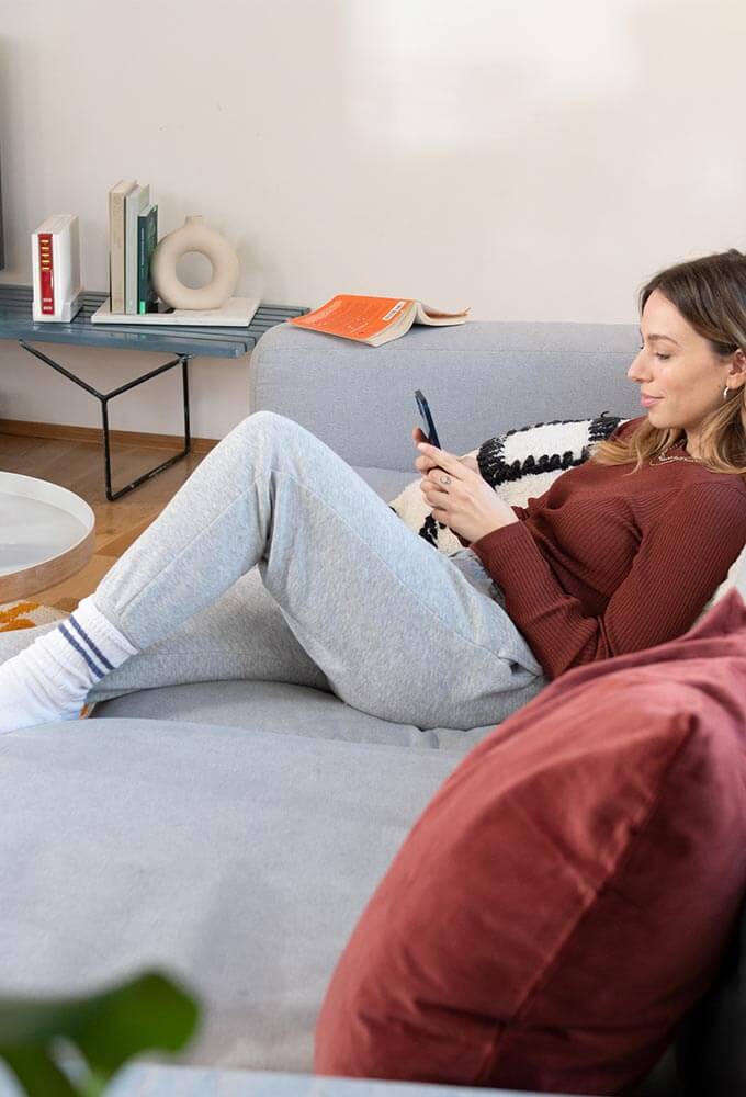 Eine Frau liegt auf dem Sofa auf ihr Handy blickend.